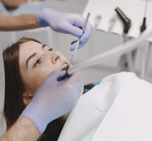 Female patient sitting in the dental chair while dentist doing e Female patient with braces has dental examination at dentist office. Woman wearing white clothes. Male dentist treats girl.